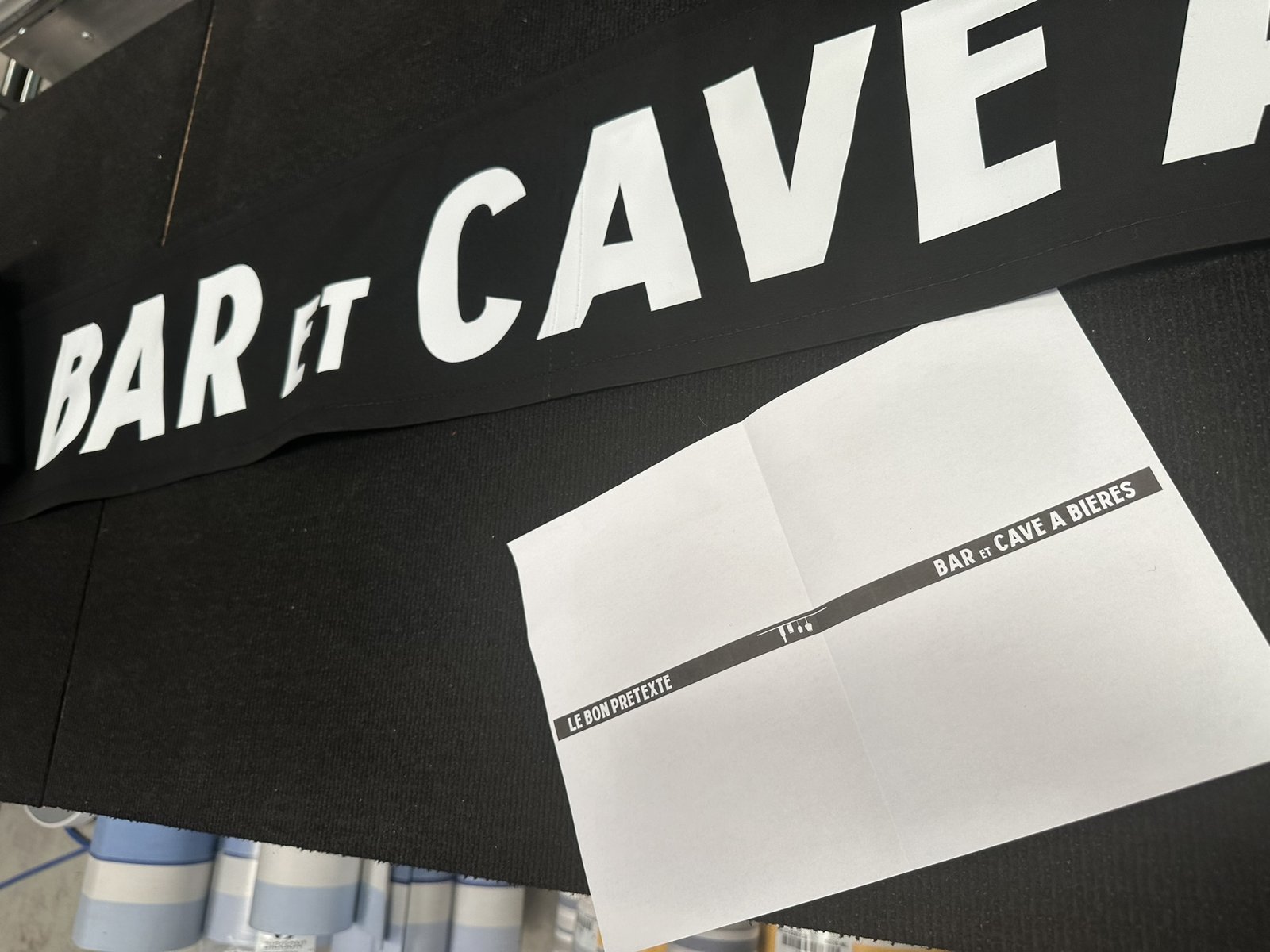 Marquage sur lambrequin : lettres blanches floquées sur une toile de store noire, bon à tirer posé à côté